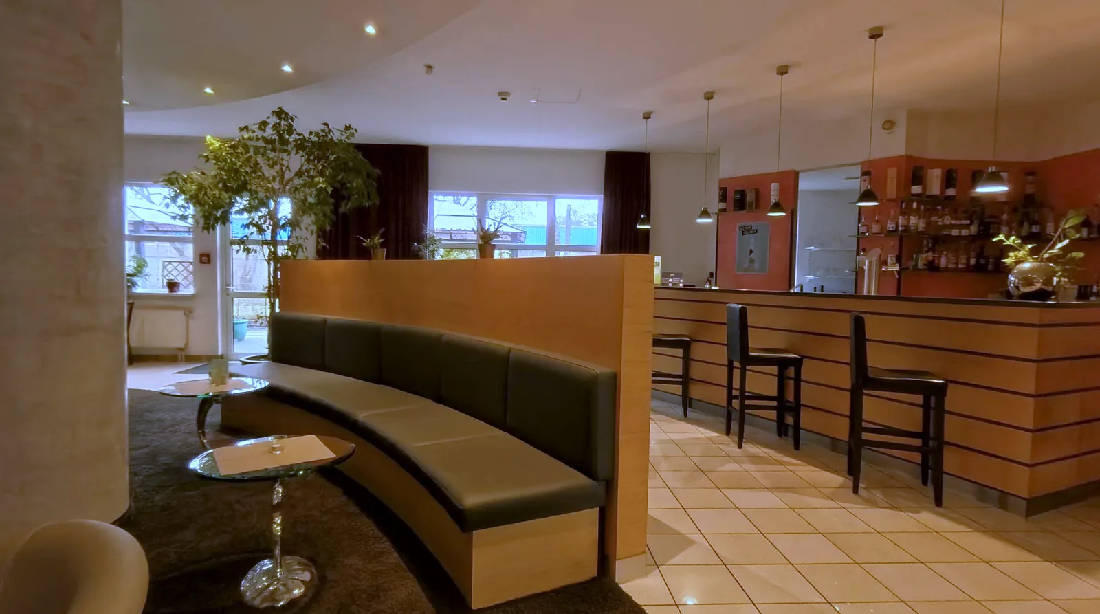 Lobby-Lounge im EURO PARK HOTEL Hennef mit geschwungener Sitzbank, kleinen Glastischen, Bartheke mit Hockern und einer Fensterreihe